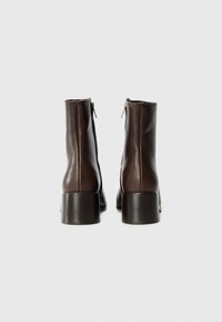Bottines en cuir marron avec une texture lisse, des fermetures éclair latérales et un talon épais. Présentent un design minimaliste et des lignes épurées.