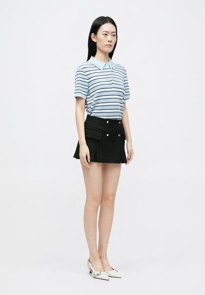 Gestreiftes blaues Poloshirt mit Kragen, kombiniert mit einem schwarzen plissierten Rock mit Taschen und goldfarbenen Knöpfen. Weiße spitze Ballerinas.