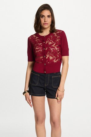 Cardigan bourgogne à manches courtes avec des détails en dentelle, boutons sur le devant, associé à un short en jean foncé avec des coutures contrastées.