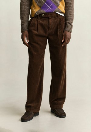 Person wearing brown corduroy pants, dark brown shoes, and a brown sweater with a yellow and purple argyle pattern.