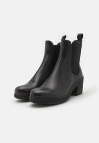 Bottines en cuir noir avec une finition lisse, des panneaux élastiques sur les côtés et un talon épais pour plus de hauteur et de soutien.