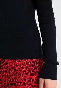 Haut noir à manches longues en tricot côtelé avec des manches ajustées, associé à une jupe à imprimé léopard rouge et rose, comportant un détail logo subtil au bas.