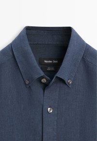 Granatowa lniana koszula na guziki z zapiętym kołnierzykiem i widoczną metką z napisem „Massimo Dutti.”