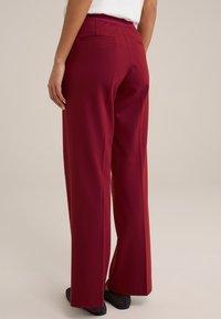 Burgundy színű, sima anyagból készült bővülő nadrág, hátul két zsebbel és magas derékkal, fekete hálós slip-on cipőkkel párosítva.