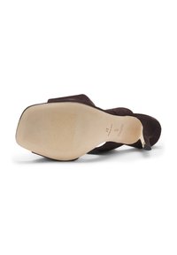 Chaussure à talon haut en daim marron posée sur le côté, montrant une semelle beige lisse avec de légères nervures et une pointe de talon pointue.