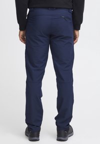 Tmavě modré venkovní kalhoty s elegantním designem, vybavené zipovou kapsou na zadní straně, vyrobené z lehké, odolné tkaniny s vyztuženými švy.