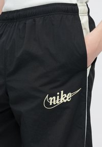 Μαύροι αθλητικοί σορτς από ελαφρύ υλικό, με ελαστική μέση, πλαϊνές τσέπες και αντίθετη λευκή ρίγα. Φέρουν το λογότυπο της Nike.