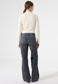 Uitlopende grijze denim jeans gecombineerd met een textuurrijke crèmekleurige top met lange mouwen, voorzien van een subtiel bladmotief en een klassieke snit.