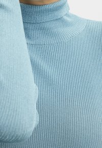 Jasnoniebieski sweter z prążkowanym kołnierzem, charakteryzujący się dopasowanym krojem i teksturowanym materiałem. Zbliżenie podkreśla detal kołnierza i rękawów.