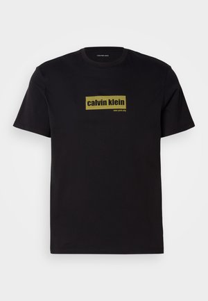 Camiseta de algodón negra con mangas cortas, que presenta un logo rectangular verde con el texto "calvin klein" y "new york city" en letras negritas.