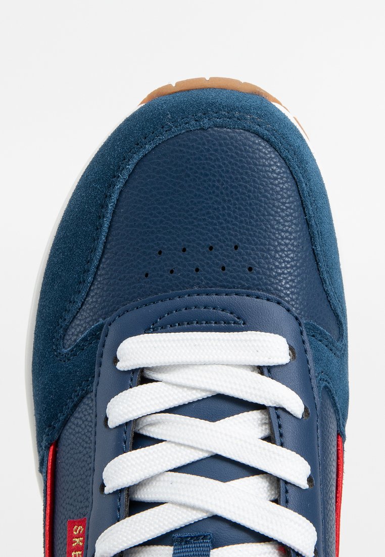 Baskets bleu marine en cuir et en suède. Lacets blancs, bout perforé et détails rouges sur le côté. Semelle en caoutchouc avec un profil marron.