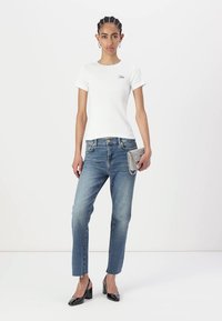 T-shirt bianca in cotone a maniche corte, jeans in denim blu medio e décolleté nere in pelle verniciata. Tiene una pochette argentata.