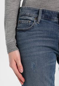 Jeans in denim blu scuro con un classico design a cinque tasche, una texture scolorita e lievi segni di usura nella zona delle cosce.