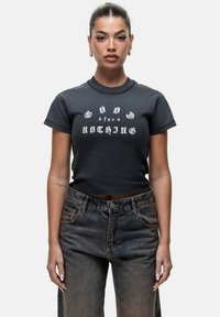 T-shirt noir court avec un texte graphique blanc indiquant « GOOD for NOTHING ». Le tissu semble doux, avec des manches courtes et une coupe classique.