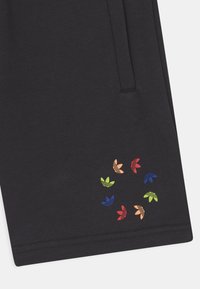 Pantaloni da jogging neri in cotone con un logo floreale circolare multicolore sulla coscia sinistra, con una texture liscia e una vestibilità rilassata.