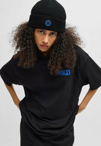 Zwarte oversized t-shirt met blauwe "HUGO" logo en zwarte ribgebreide beanie met een glimlach ontwerp. Zacht katoenmateriaal met een ontspannen pasvorm.