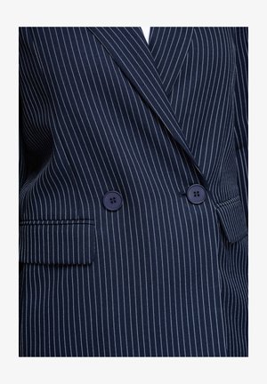 Marineblauw dubbelgeknoopt colbert met dunne witte krijtstrepen, twee donkere knopen en klepzakken.