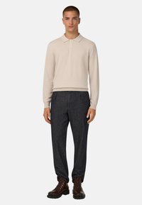 Beige Langarm-Polohemd mit Kragen, kombiniert mit dunklen Jeans und braunen Schnürstiefeln. Einfaches Design mit einer klaren Silhouette.