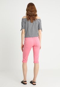 Top de cuadros en blanco y negro, con los hombros al aire y mangas cortas, combinado con pantalones capri rosa enrollados y sandalias negras.