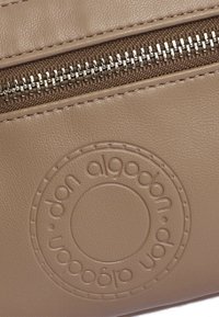 Bolso de cuero marrón claro con una superficie texturizada, un logotipo en relieve prominente y una cremallera plateada en un panel de tela en contraste.