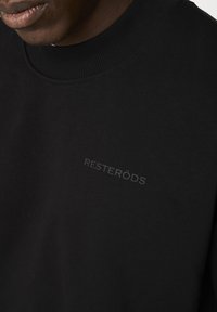 Sort sweatshirt med ribbet halsudskæring. Har et subtilt, præget logo "RESTERÖDS" på forsiden. Glat stofstruktur.