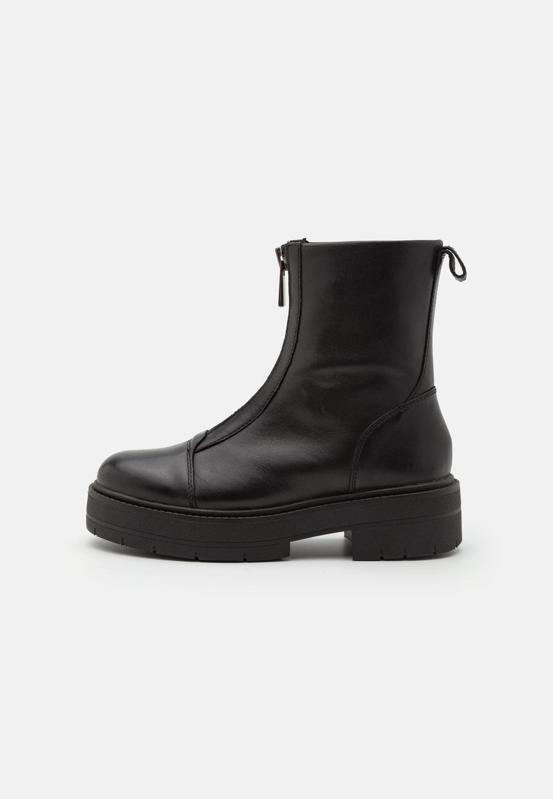 Botte noire à la cheville en cuir brillant. Présente un bout arrondi, une fermeture éclair sur le côté, et une semelle épaisse et texturée avec des rainures profondes pour une meilleure adhérence.
