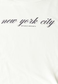 T-shirt en coton blanc avec un imprimé texturé noir de "new york city" et "STUDIO SOCIETY" en petite police en dessous.