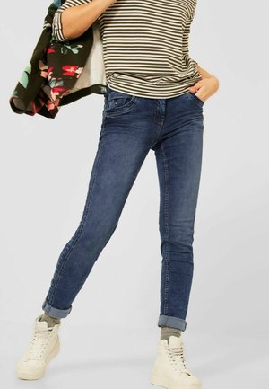 Jean en denim bleu foncé, coupe slim, avec un design classique à cinq poches, associé à un haut rayé et des baskets montantes blanches.