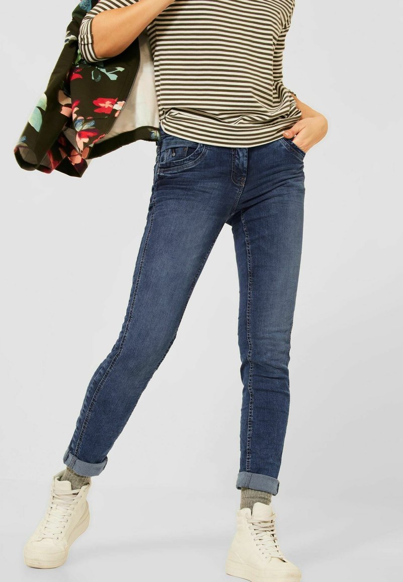 Mörkblå denimjeans med smal passform, med en klassisk femficksdesign, och matchade med en randig topp och vita hög högdämpade sneakers.