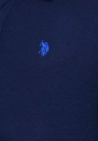 Granatowa koszulka polo z teksturowanej tkaniny, z małym, niebieskim haftowanym logo jeźdźca z kijem po lewej stronie piersi.