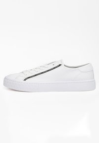 Sneaker bianchi a basso profilo con design stringato, suola testurizzata e striscia nera con il logo "GUESS" ripetuto lungo il lato.