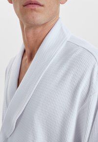 Bata blanca de punto waffle con cuello de chal, que presenta una superficie texturizada, vista desde la zona del cuello y el hombro.