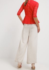 Haut en dentelle rouge à peplum avec des manches trois-quarts, associé à un pantalon large crème. Détail de fermeture éclair à l'arrière du haut. Talons neutres.