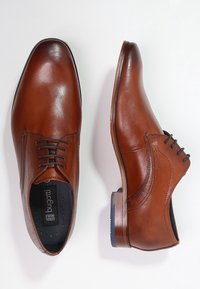 Chaussures habillées pour hommes en cuir marron avec des lacets noirs, l'une vue de dessus et l'autre vue de côté, sur un fond blanc.