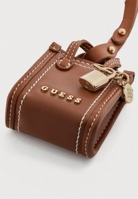 Braune Kunstleder-Mini-Handtasche mit weißen Nähten, goldenen Beschlägen und einem Vorhängeschloss. Markennamen "GUESS" auf der Vorderseite geprägt.
