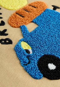 Gros plan d'un chien bleu texturé avec un œil jaune et un nez noir à côté d'une miche de pain orange sur un tissu beige. Texte noir partiellement visible.