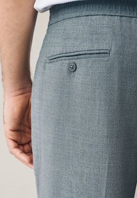 Hellgraue Hose aus strukturiertem Stoff, mit einer Gesäßtasche und Knopfverschluss. Das Design zeichnet sich durch eine saubere, maßgeschneiderte Optik aus.