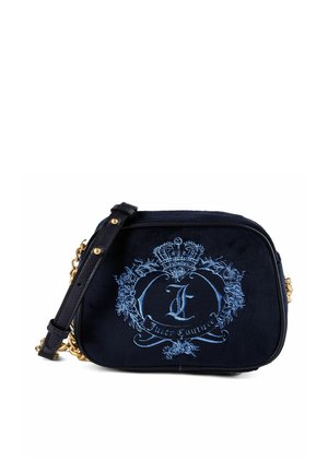 Borsa Juicy Couture nera con stemma ricamato blu, corona, rose e tracolla a catena dorata su sfondo bianco.
