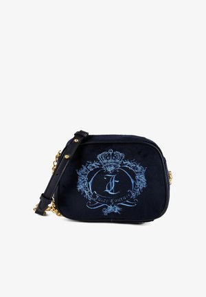 Sac noir Juicy Couture avec blason brodé bleu, couronne, roses et bandoulière chaîne dorée sur fond blanc.