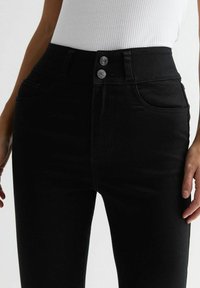 Jean en denim noir taille haute avec une texture lisse, fermeture à deux boutons et poches avant avec de subtils détails de couture.