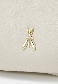 Material de cuero beige con superficie texturizada; presenta un acento dorado en forma de insecto con alas, adjunto a la esquina inferior derecha.