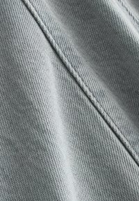 Gros plan sur un tissu en tricot gris avec une couture diagonale visible et un détail de couture texturée.