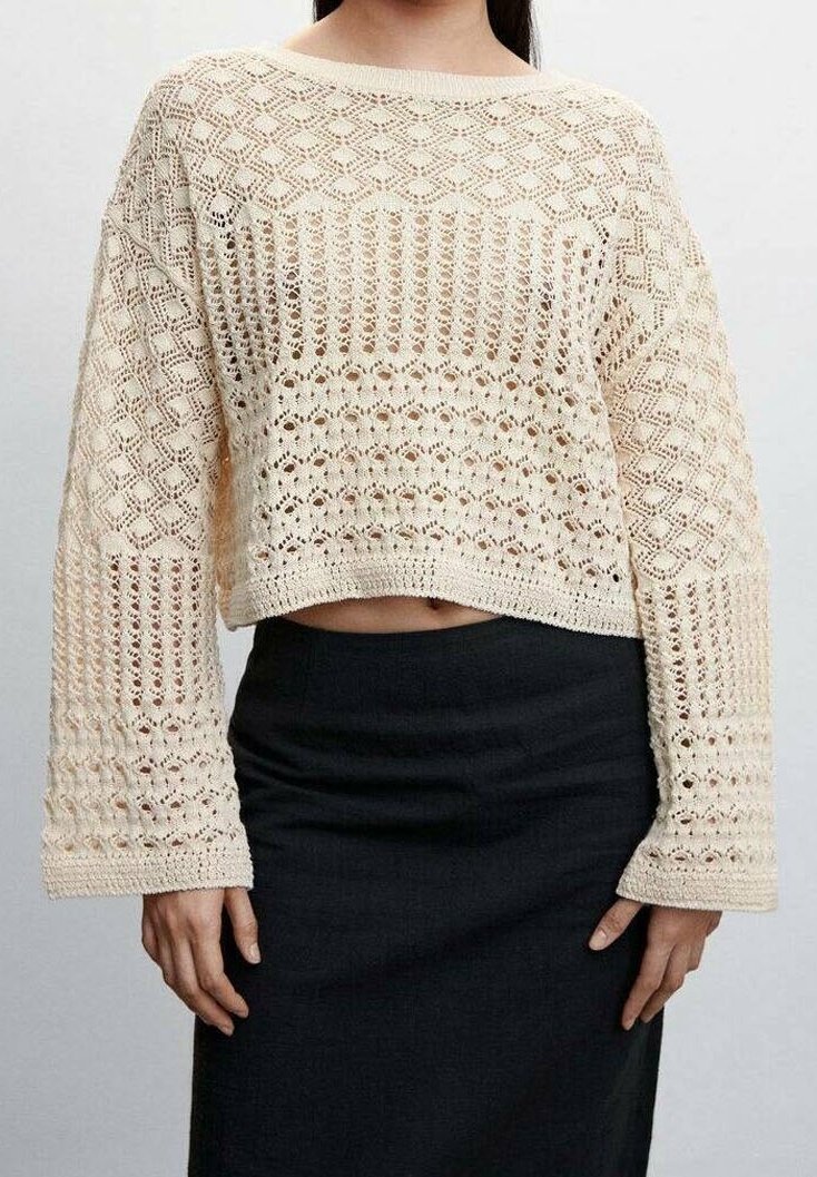 Cremfarbener Häkelpullover mit weiten Ärmeln, der mit texturierten Mustern und einem verkürzten Saum versehen ist, kombiniert mit einem figurbetonten schwarzen Rock.