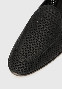 Μαύρο παπούτσι τύπου slip-on με διάτρητη επιφάνεια και στρογγυλεμένη μύτη. Διαθέτει ομαλή εξωτερική άκρη και ευέλικτη σόλα.