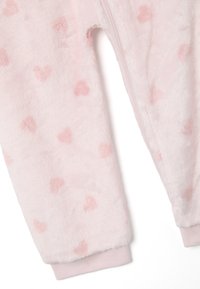 Rosa Fleece-Einteiler mit weichem, plüschigem Material und herzförmigen Mustern in helleren Rosa-Tönen. Enthält einen Reißverschluss und gerippte Bündchen.