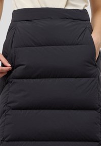 Gevulde zwarte outerwear met een gestructureerde afwerking, met een hoge taille en ritszakken aan de zijkanten, ontworpen voor warmte en comfort.