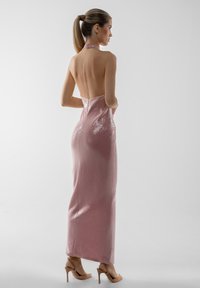 Ruža halter haljina s otvorenim leđima, teksturiranim sjajnim detaljima i uskim siluetom. Uparena s nude sandalama na visoku petu.