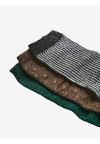 Tres pares de calcetines: uno verde, uno marrón con un patrón de puntos y uno a rayas en negro y blanco, todos con una textura brillante.