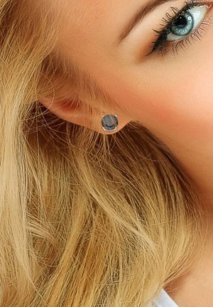 Boucles d'oreilles rondes en métal avec une pierre grise facettée, comportant quatre griffes, présentées sur un fond de cheveux clairs.