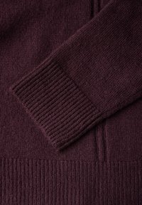 Burgundy stickad tröja med ribbstickade ärmar och en slät yta. Tyget verkar mjukt och visar en lätt variation i mönster och färgdjup.